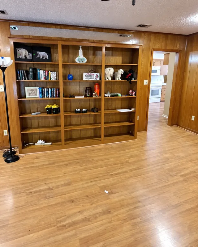 Books, framed pictures and ornaments on built-in wooden shelves before removal; camera angle aligned with AI