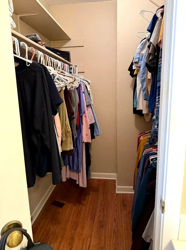 A walk-in closet packed with hanging clothes on both rails before clearing