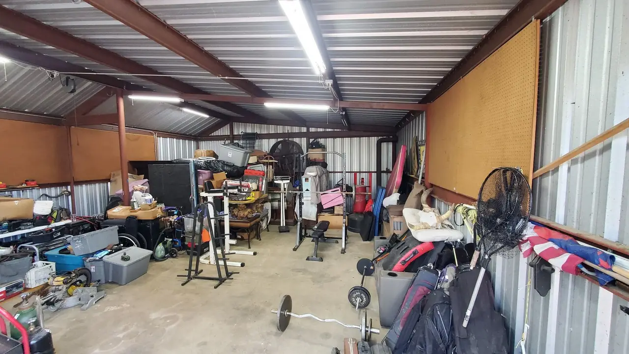 The same metal shop partway through clearing, with the concrete floor visible down the centre and remaining items stacked along the walls